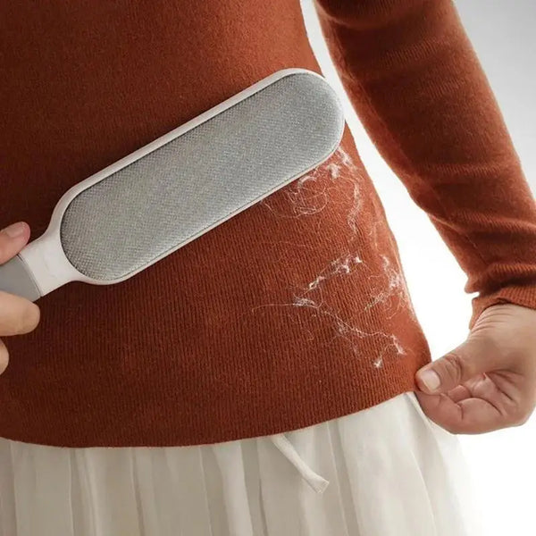Person brushing visible pet hair off a sweater using a double-sided pet hair remover brush.
